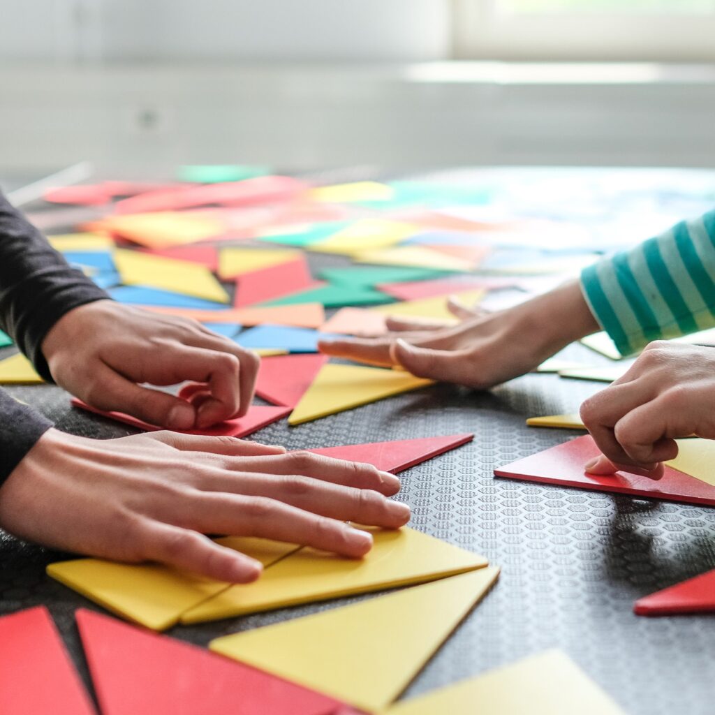 Hände legen bunte Dreiecke aus Pappe auf eine schwarze Unterlage mit Rastermuster.