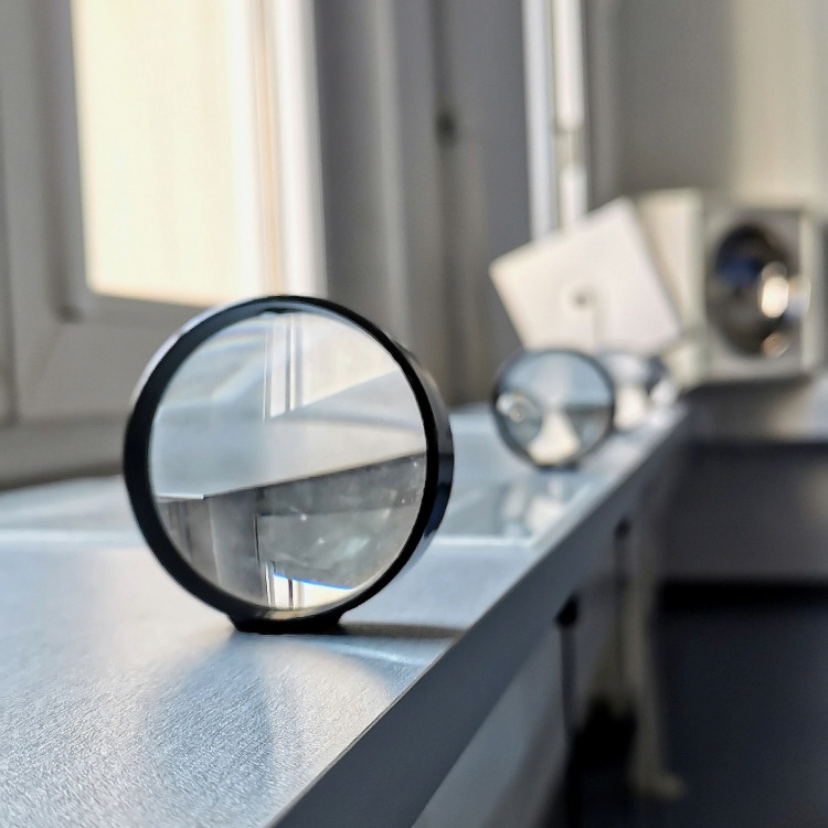 Runde Lupe auf Fensterbank, im Hintergrund weitere Lupen unscharf sichtbar.
