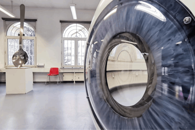 Großes, rundes Gerät mit transparentem Ring in hellem Raum mit Fenstern und rotem Stuhl.