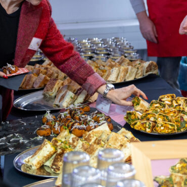 Gefüllte Wraps mit Salat und Gemüse auf einem Buffet, im Hintergrund unscharfe Personen bei einer Veranstaltung.