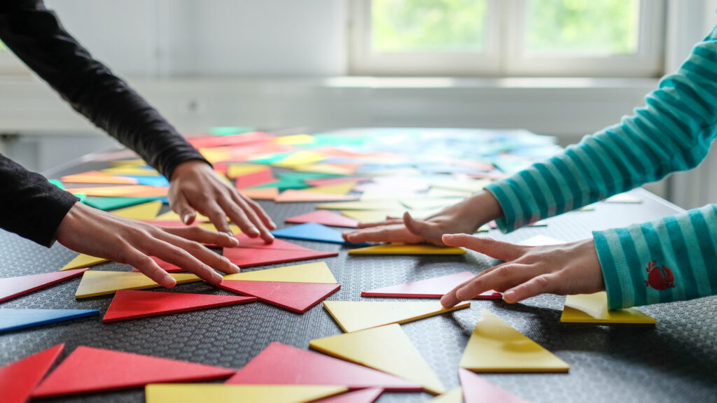 Hände legen bunte Dreiecke aus Pappe auf eine schwarze Unterlage mit Rastermuster.