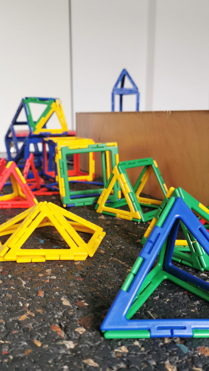 Bunte dreidimensionale geometrische Formen aus Kunststoffstäben auf dunklem Untergrund, darunter Pyramiden und Würfel.