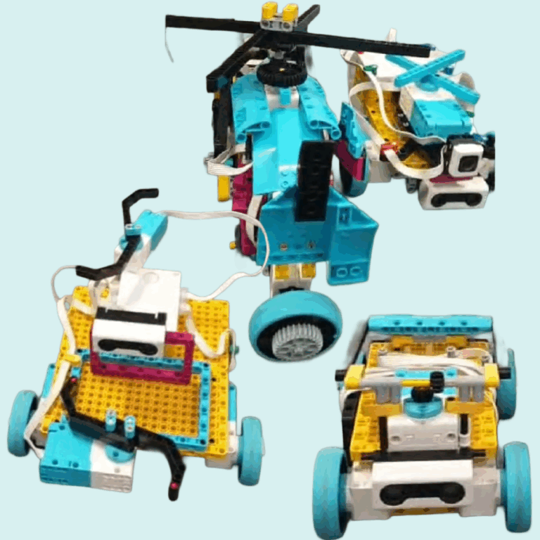Drei verschiedene blaue und gelbe Lego Spike Robotermodelle mit Rädern und Sensoren, angeordnet auf einer Fläche.