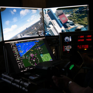 Cockpit eines Flugsimulators mit digitalen Instrumentenanzeigen und einer Panoramaansicht einer Stadt am Himmel auf mehreren Bildschirmen.